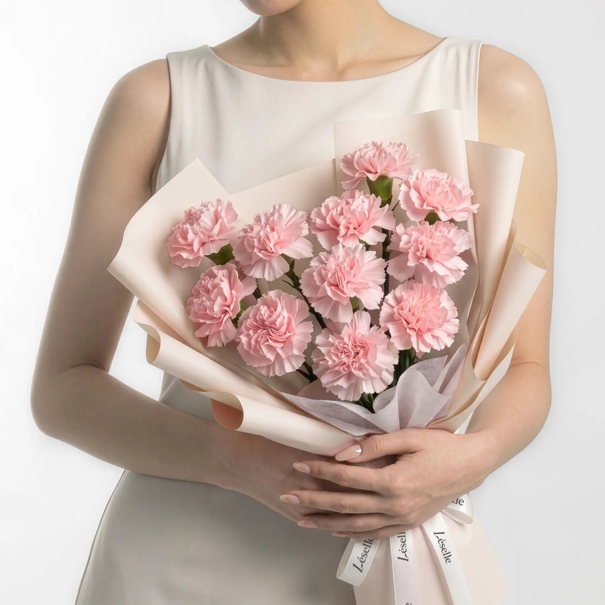 Bouquet of soft pink carnations held by a person in a white dress on a white background